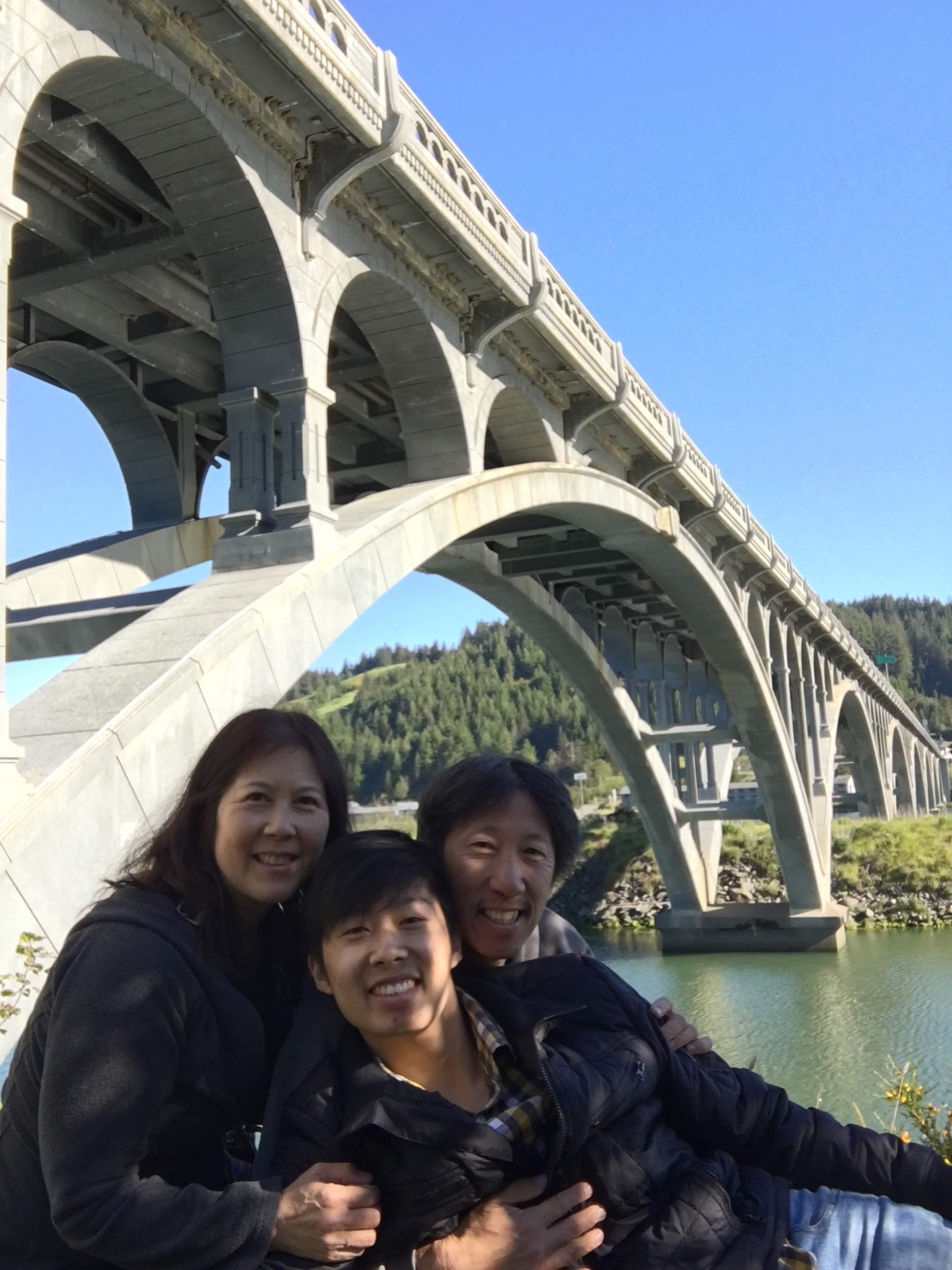 louie family posed in front of a beautiful bridge along oregon's coast